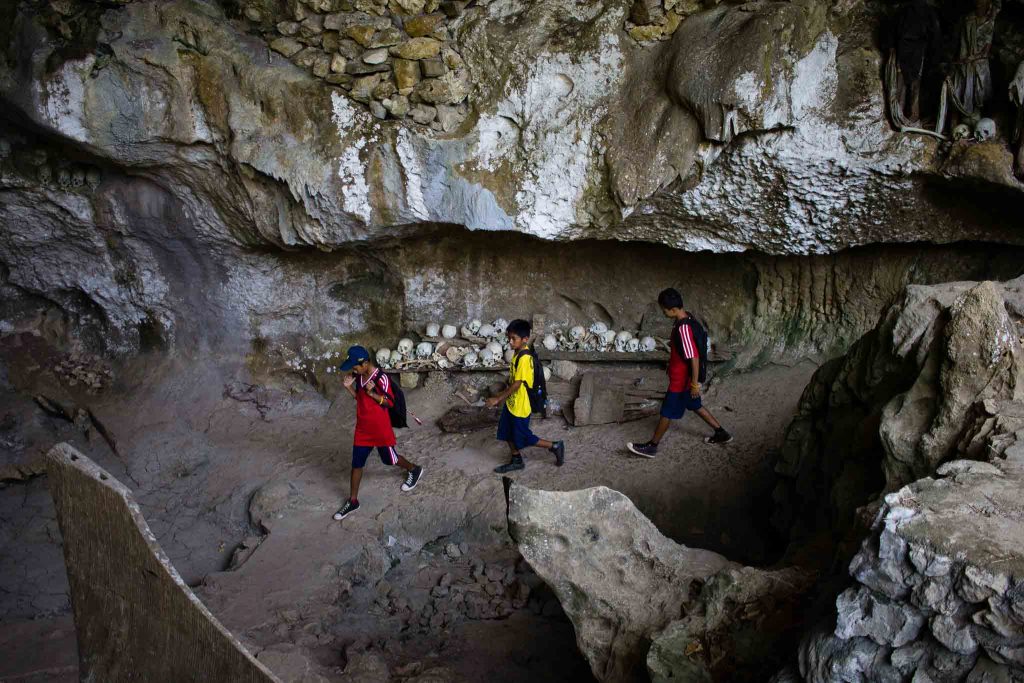 Niños pasan por una cueva con calaveras usada como cementerio en Tana Toroja Indonesia