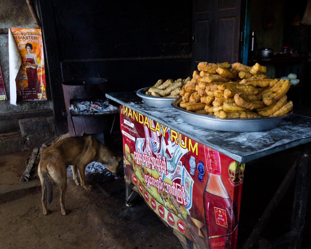 Mercado callejero en Myanmar donde se ve un perro y un puesto de churros