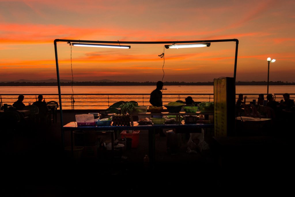 Hombre en un puesto callejero al atardecer con un rio al fondo