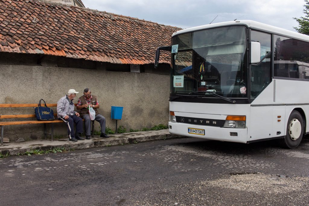 Dos hombres en un banco en una estación al aire libre con un autobús al lado
