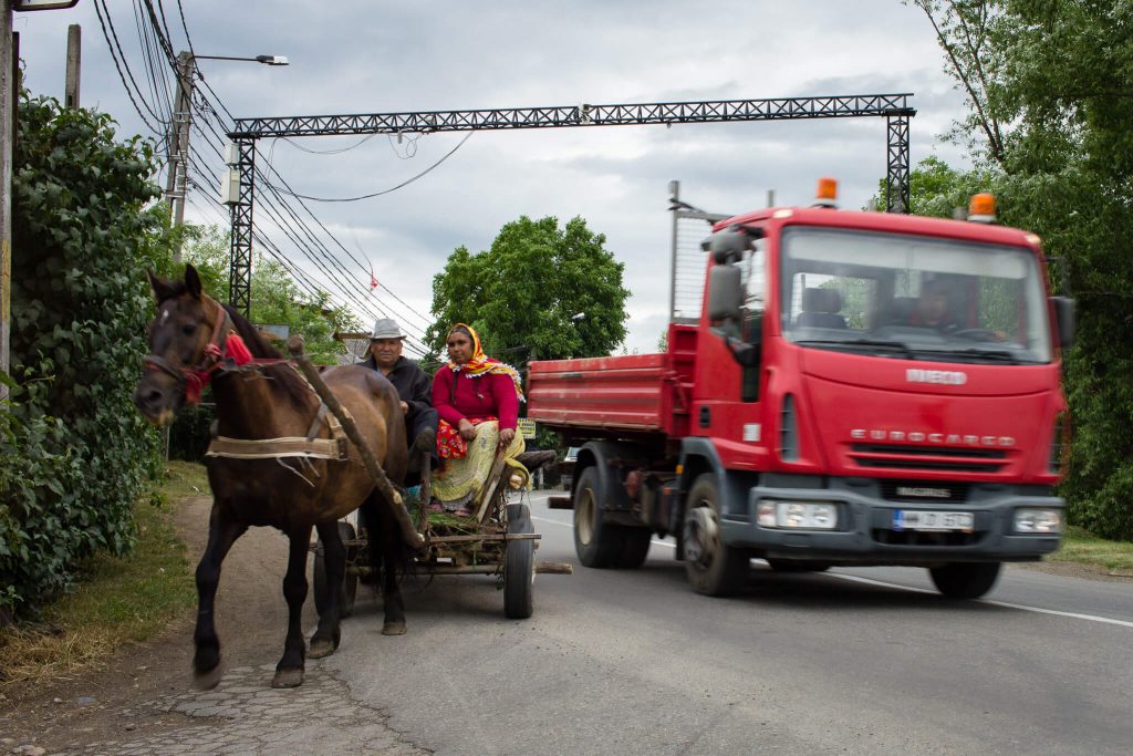 Carretera en Rumanía con una pareja de romas en el un carro de caballos y un camión rojo pasando al lado