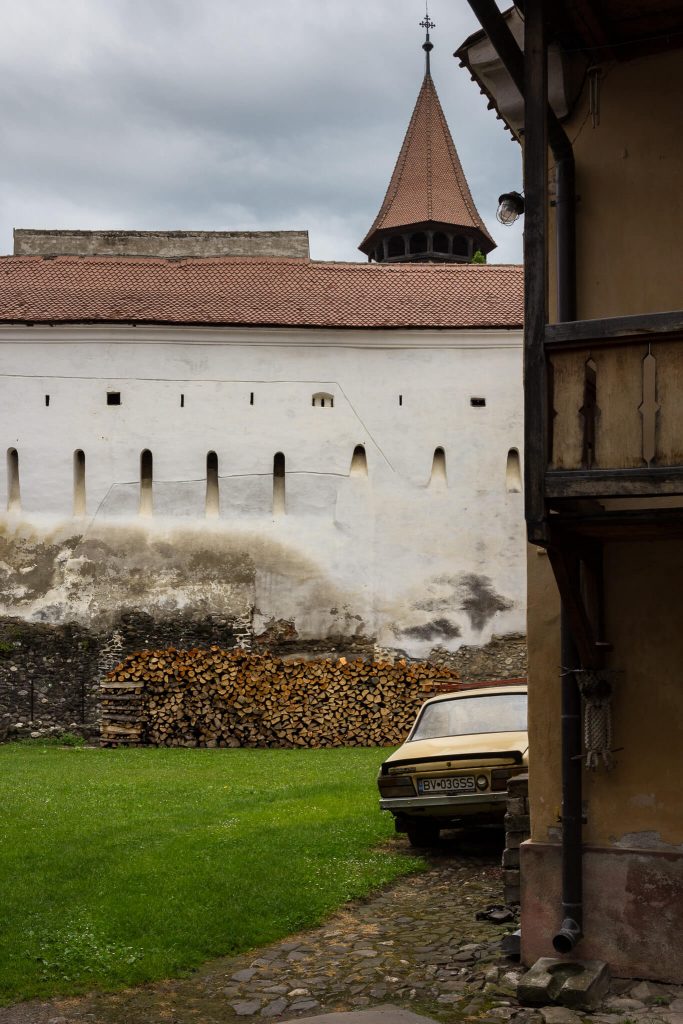 Patio de una iglesia fortificada en Transilvania Rumanía, donde hay almacenada madera y un coche amarillo antiguo