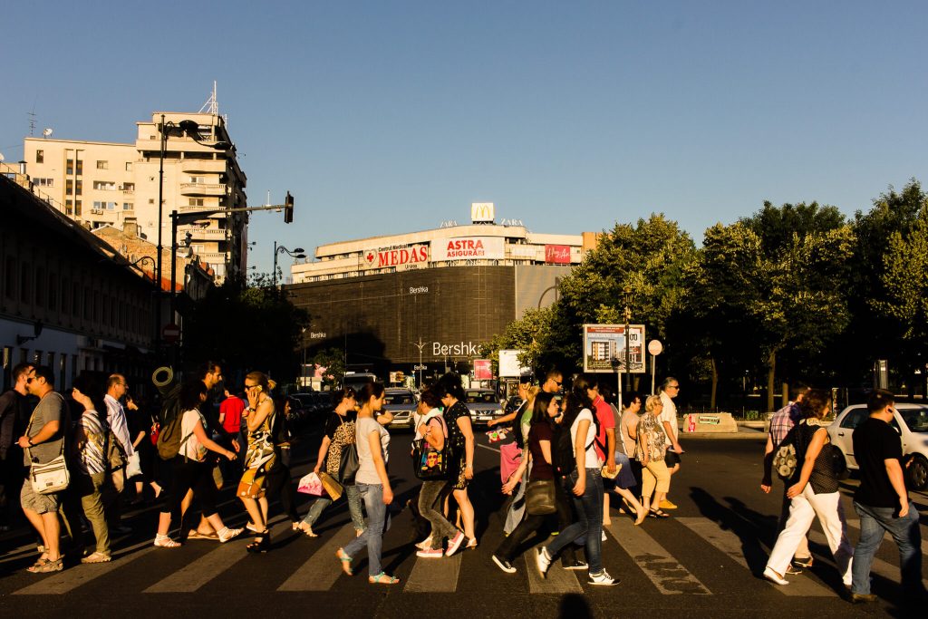 Gente cruzando un paso de peatones en un atardecer en Bucarest con un centro comercial al fondo